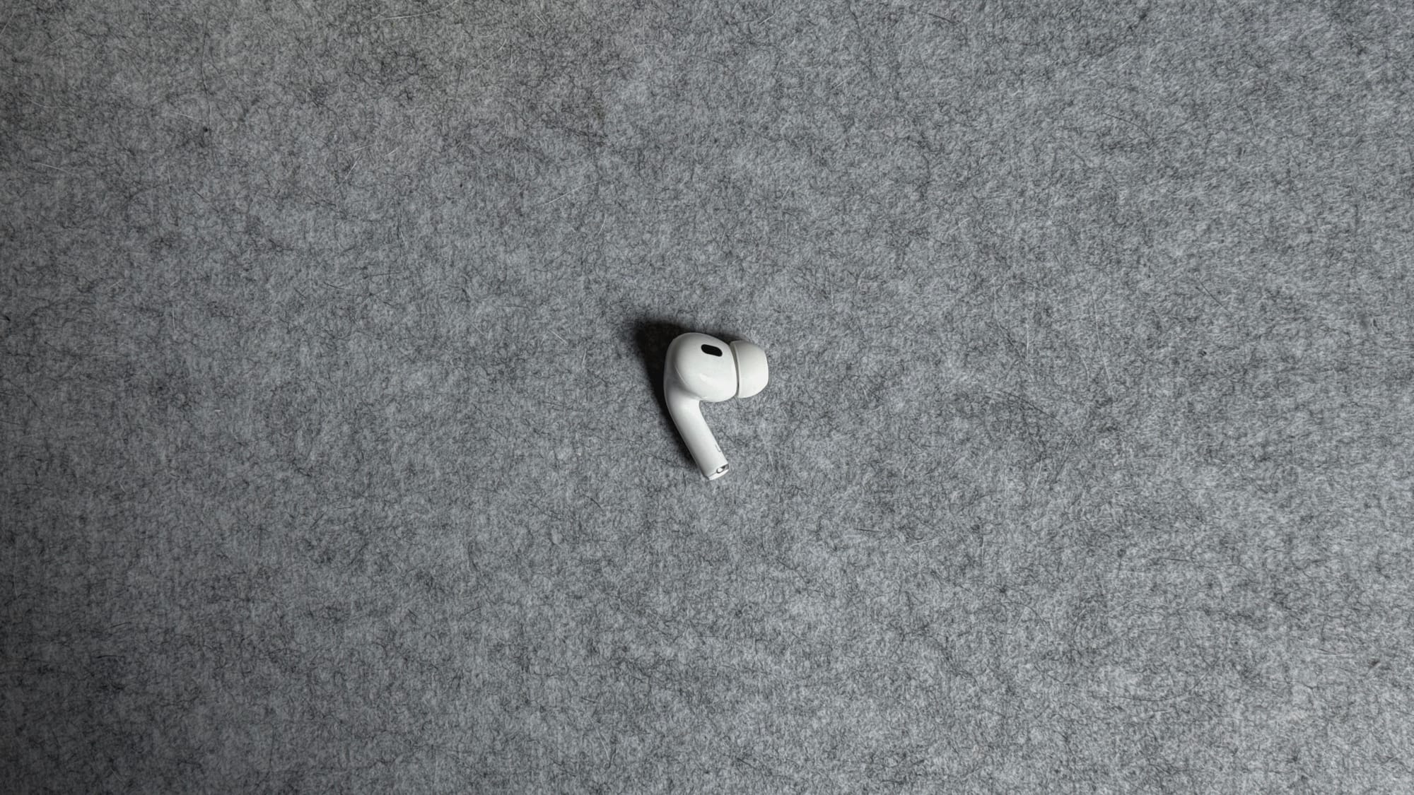 A photo of my left AirPod, lying on a grey felt desk mat